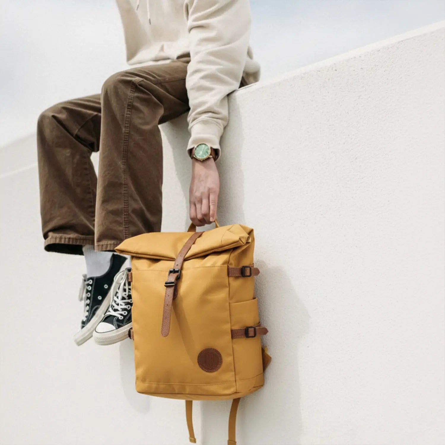 Person holding a mustard yellow backpack with brown straps on a light background