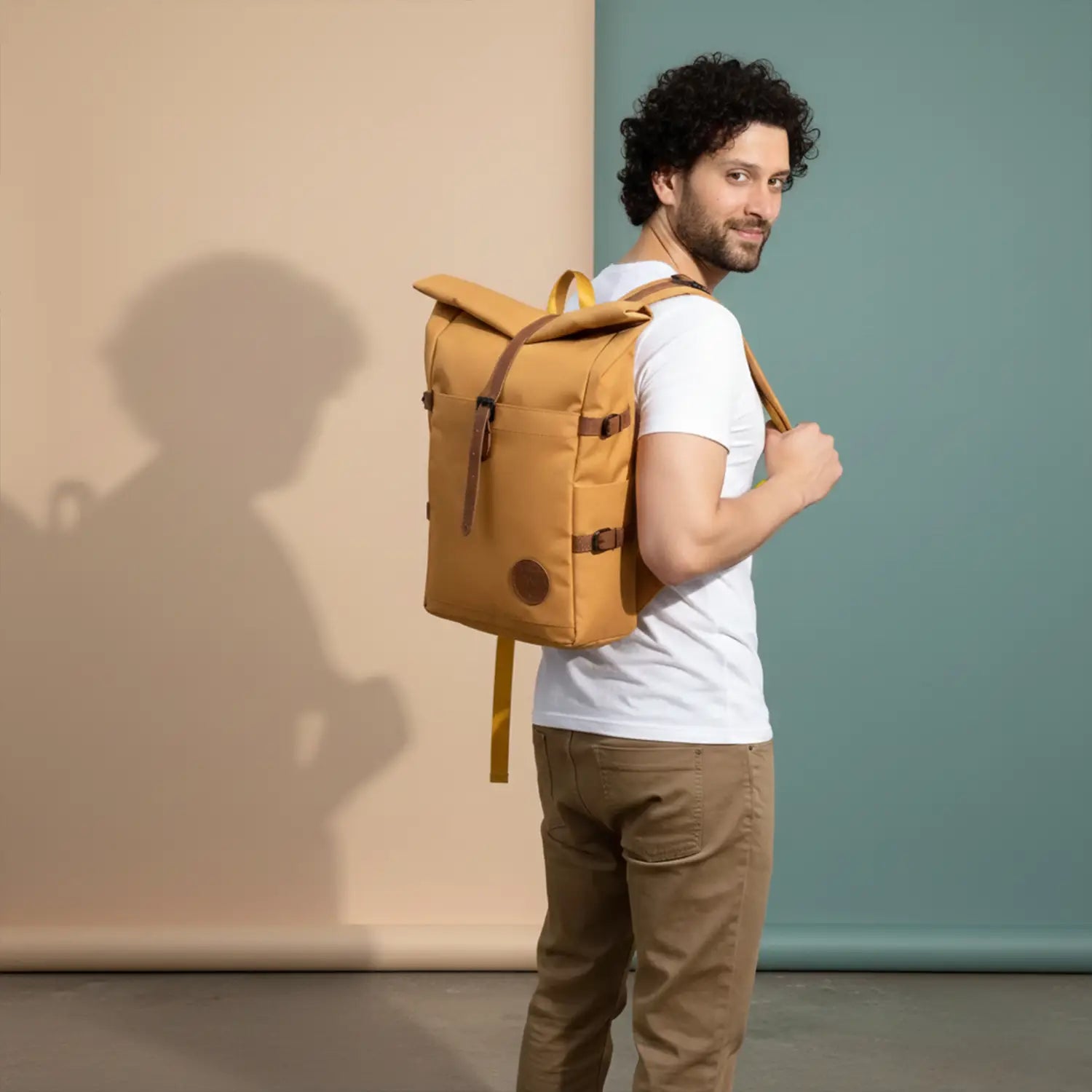 Man wearing a mustard backpack against a plain background
